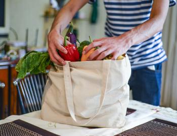 man with bag of groceries unpacking fresh produce onto counter top in kitchen