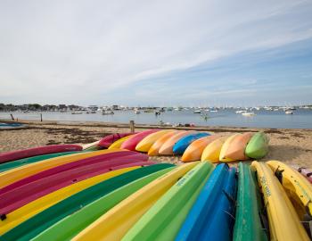 brightly colored kayaks face down in the sand on a beach in nantucket