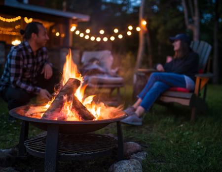 two people at bonfire outside with lights stringing from the home behind them