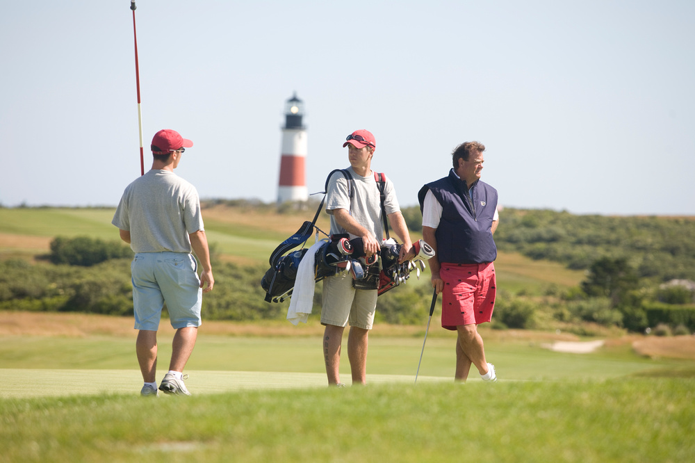 three guys on a golf course on a sunny afternoon with lighthouse in the background